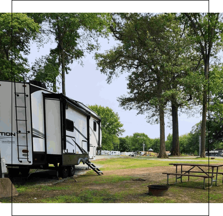 A white trailer parked in the grass near some trees.